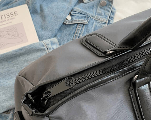 Close-up of waterproof large shoulder handbag in nylon, ideal for unisex fitness and travel, next to a denim jacket and book on a chair.