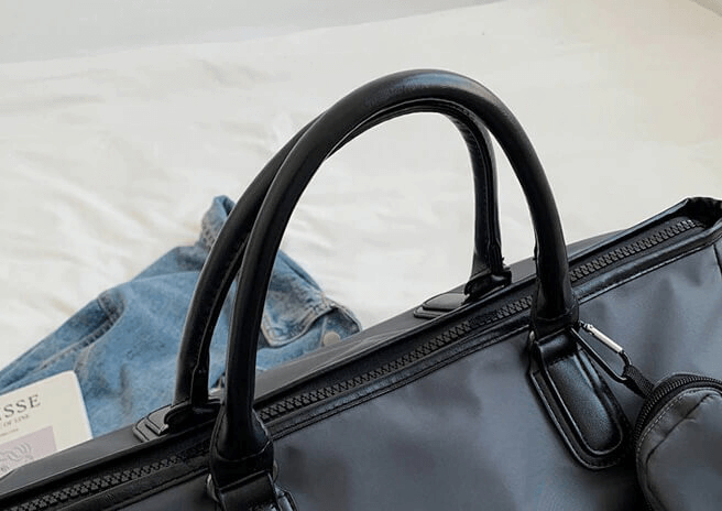 Stylish waterproof large shoulder bag in black nylon on a bed with jeans and a book. Perfect unisex sports handbag for fitness or travel.