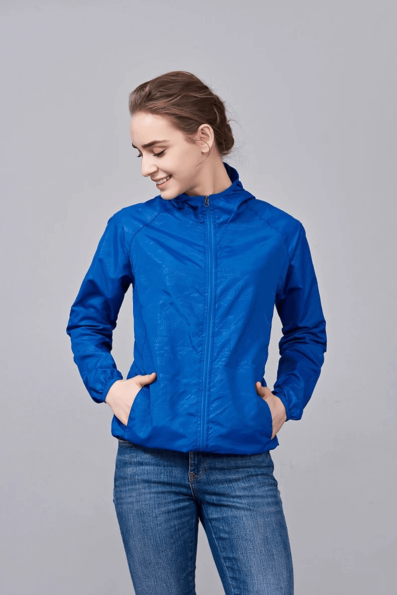 Woman wearing a blue waterproof polyester jacket for hiking, featuring breathable and sun-protective material, ideal for outdoor activities.