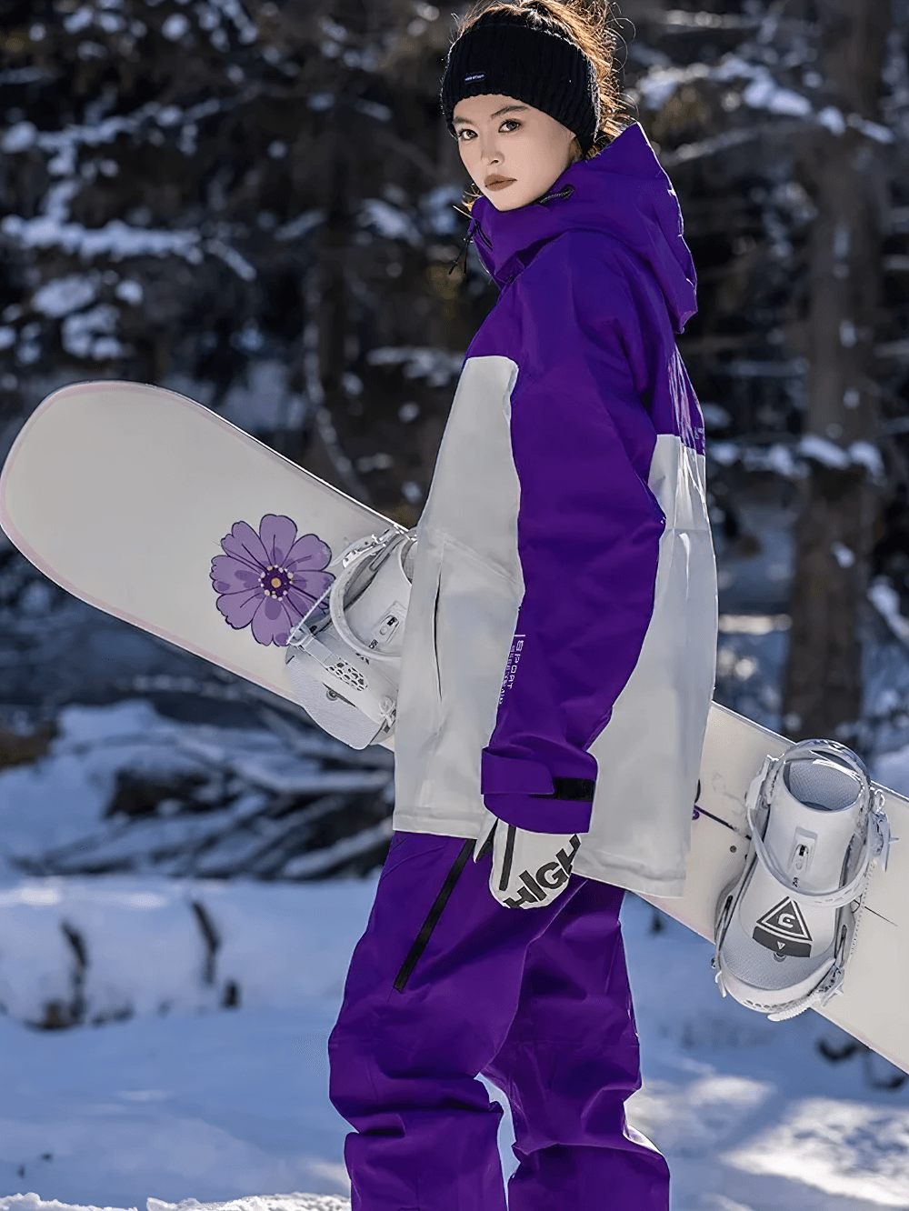 Woman in waterproof snowboarding jacket and pants SF2499 holding a snowboard in snowy forest, ready for winter adventures.