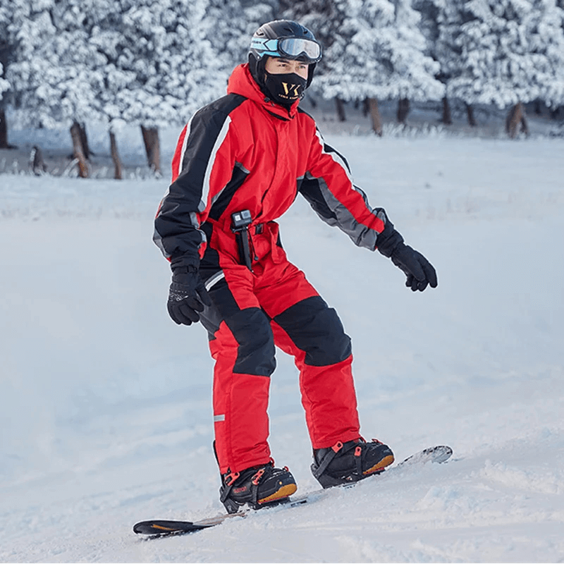 Man in red waterproof ski jumpsuit snowboarding, featuring fleece lining and windproof design for winter sports.