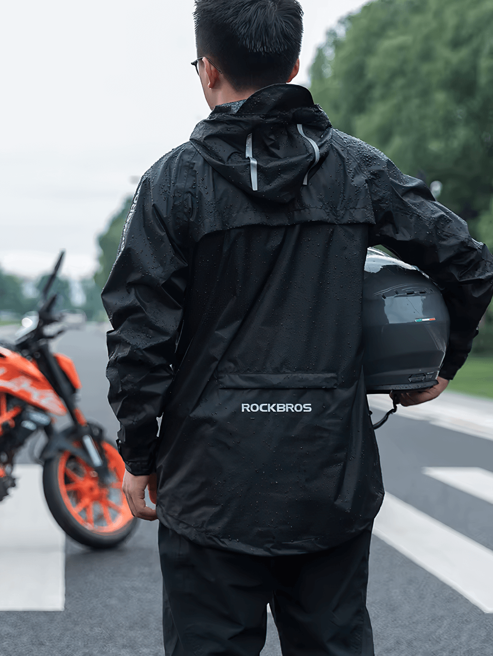 Man wearing a waterproof cycling jacket, standing on the road with a motorcycle, showcasing the durable design in rainy weather.