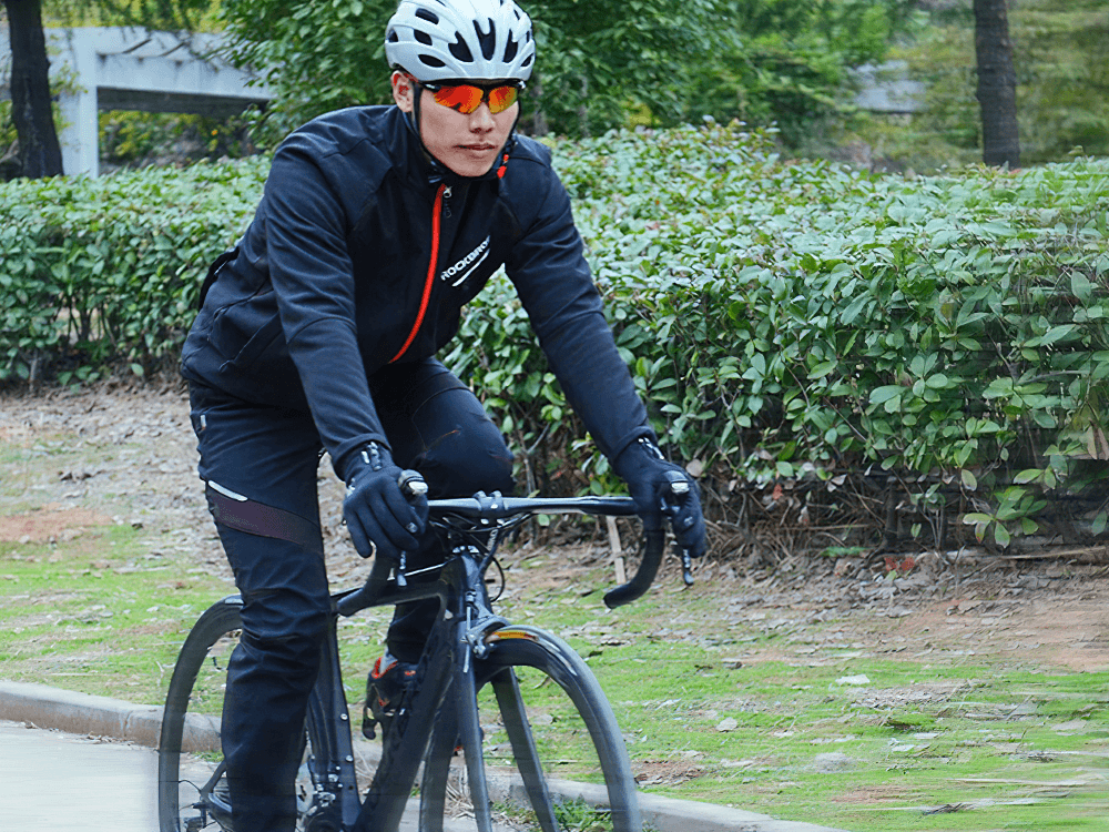 Cyclist wearing SF2638 waterproof windproof jacket and pants set with reflective detailing and helmet biking outdoors.