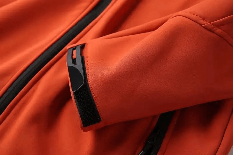 Close-up of weather-resistant softshell hooded jacket sleeve in orange with black zipper, ideal for outdoor activities.