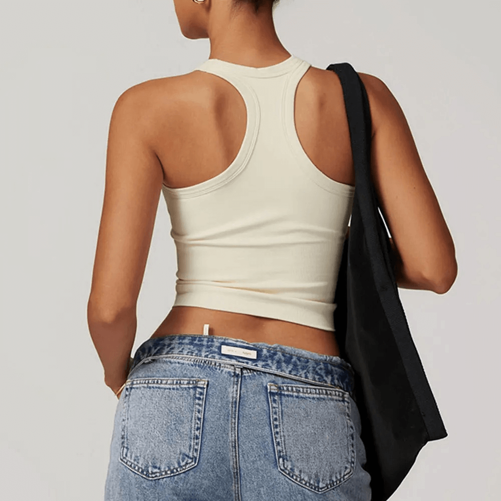 Back view of woman wearing beige racerback fitness tank top with denim jeans, showcasing breathable and quick dry material.