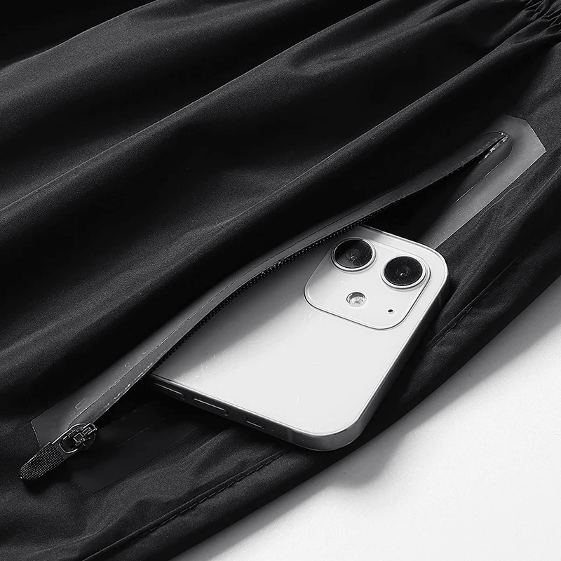 Close-up of a smartphone in a zippered pocket of a women's black quick-dry fitness tracksuit.