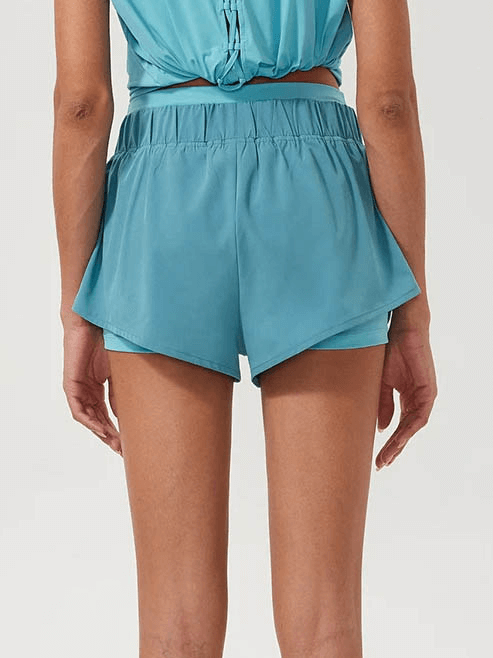 Woman wearing teal 2-in-1 athletic shorts with pockets from behind, showcasing breathable fabric and elastic waistband for running.