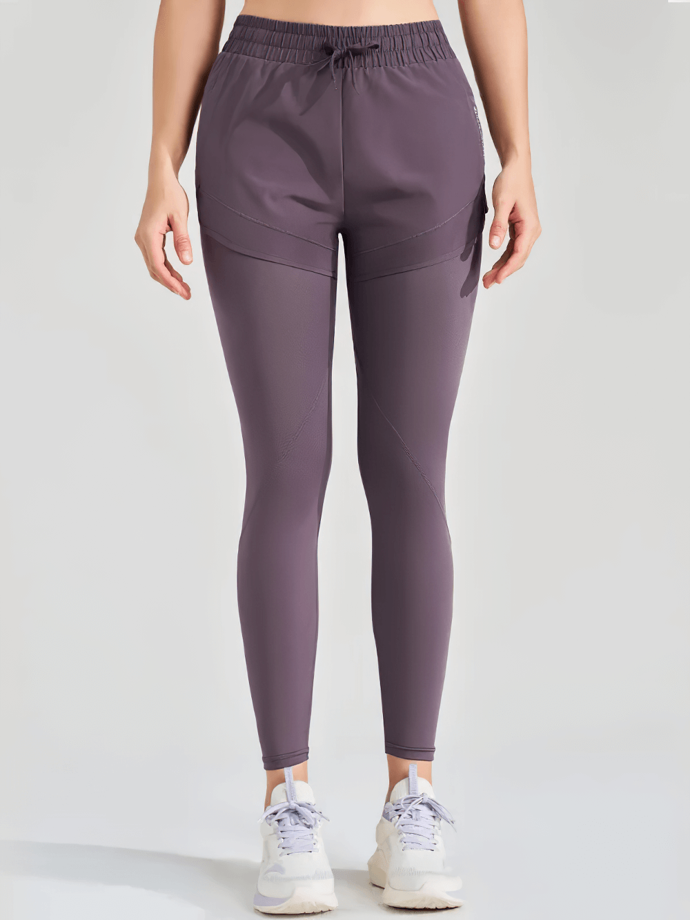 Woman wearing ankle-length fake two-piece yoga pants with elastic waist and utility pockets, perfect for running and fitness.