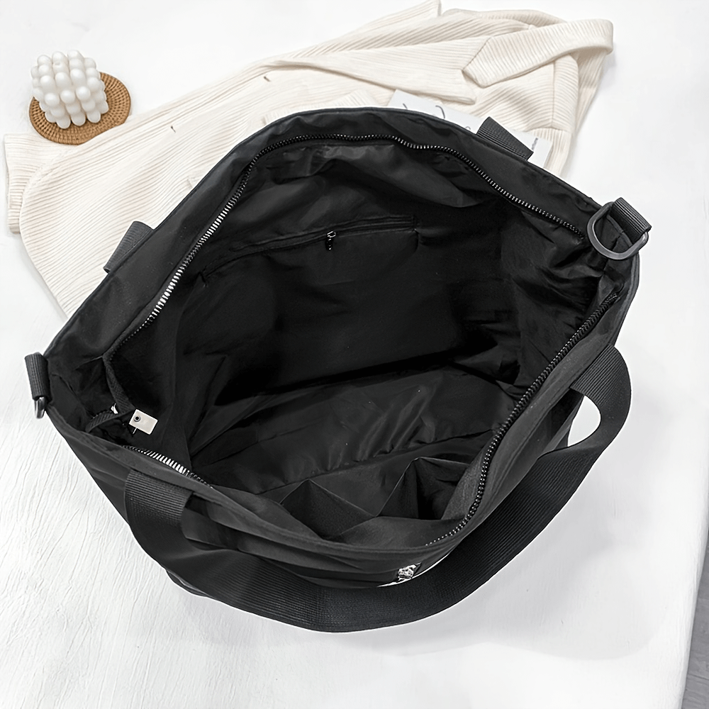 Large black nylon tote bag with spacious interior and adjustable strap, ideal for travel and everyday use. Secure zippered closure.