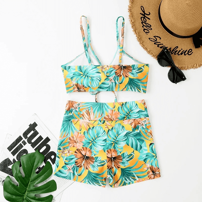Women's flower print two-piece bathing suit with tropical design, laid out next to a sunhat and sunglasses.