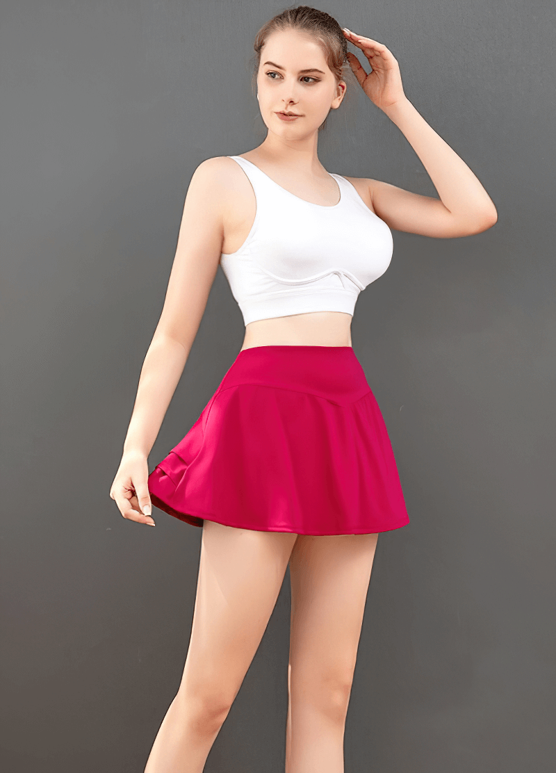 Woman wearing pink pleated shorts-skirt with inside pocket, designed for golf and tennis, showcasing stretchable and breathable material.