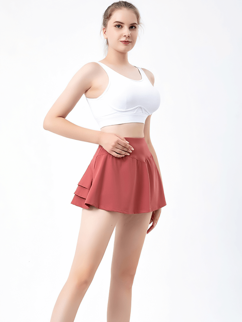Women's pleated tennis skirt in red with inside pocket, worn by model, showcasing comfort and mobility for sports activities.