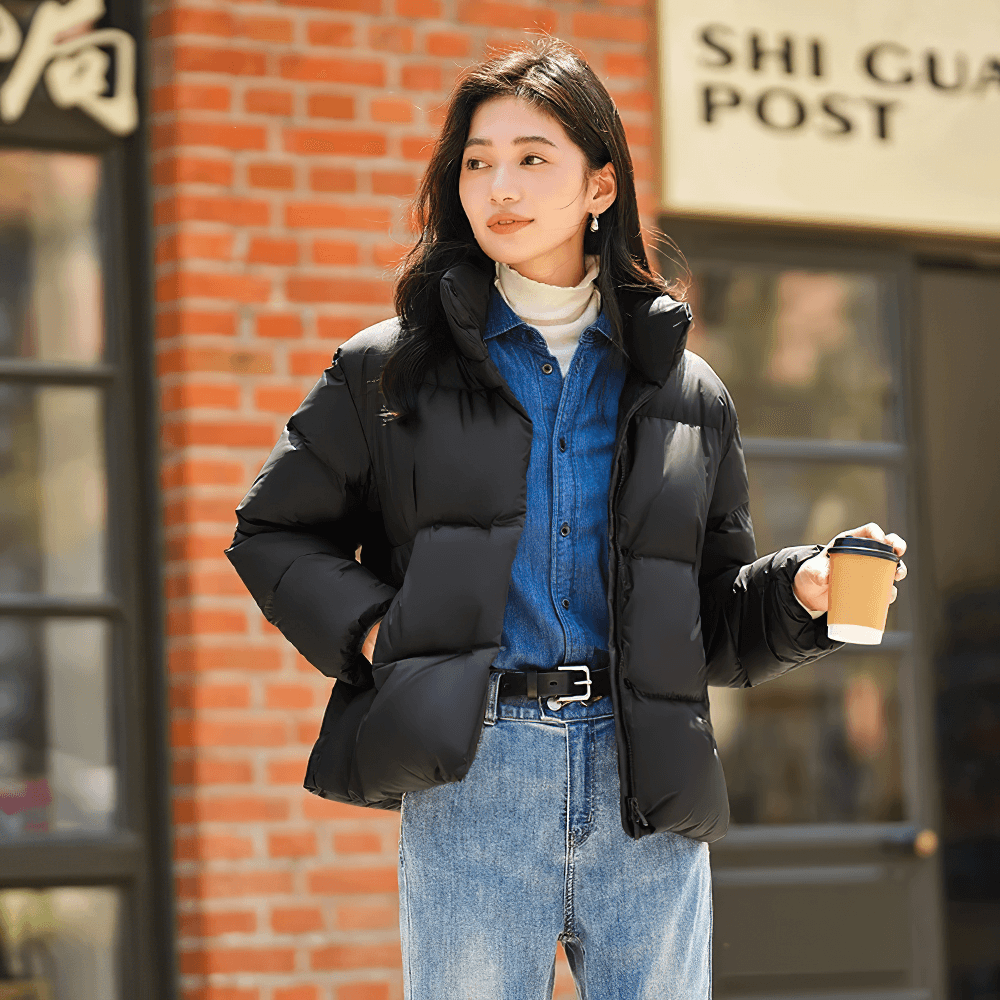 Woman wearing black women's goose down jacket with stand-up collar, holding coffee outdoors.