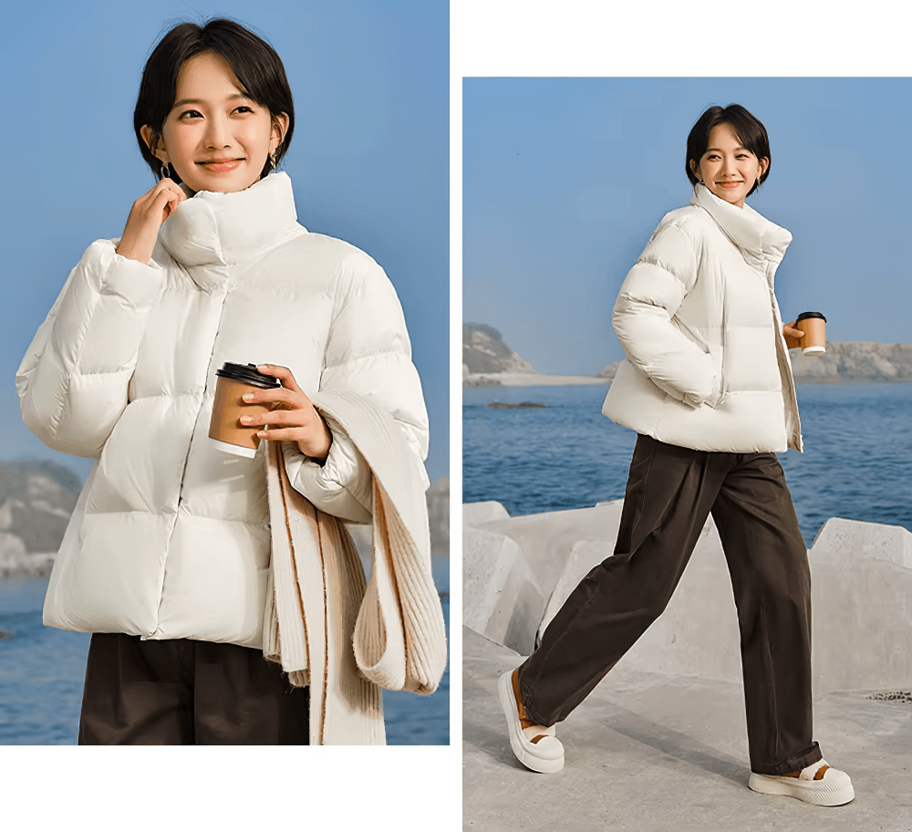 Woman wearing white goose down jacket with stand-up collar by the sea, holding coffee. Casual winter fashion.