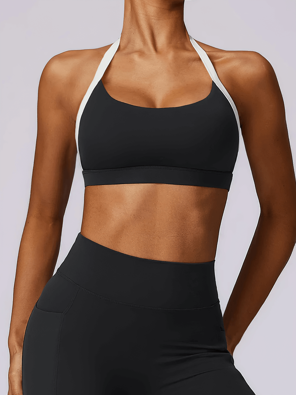 Woman wearing a stylish black halter sports bra with white contrast trim, perfect for yoga and light workouts.