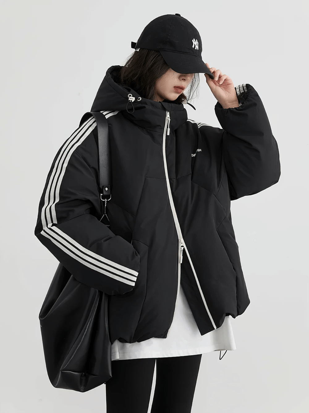 Stylish woman in black hooded striped down jacket with streetwear vibe, loose fit, and full sleeves, perfect for winter warmth.