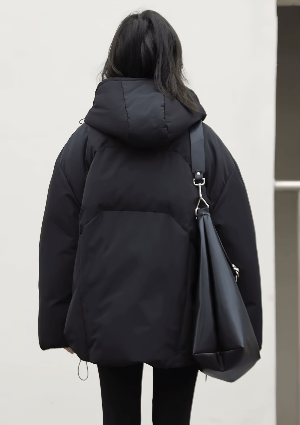 Back view of woman wearing a black hooded winter duck down jacket with a loose fit, carrying a stylish bag.