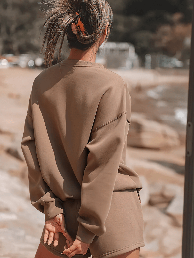 Woman wearing a stylish letter embroidery solid color sweatshirt and shorts set on beach, casual and chic summer outfit.