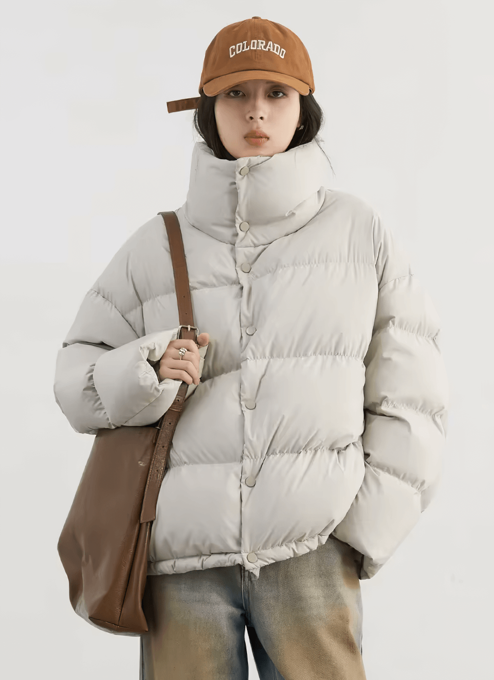 Woman wearing a white duck down winter jacket with stand collar and carrying a brown bag