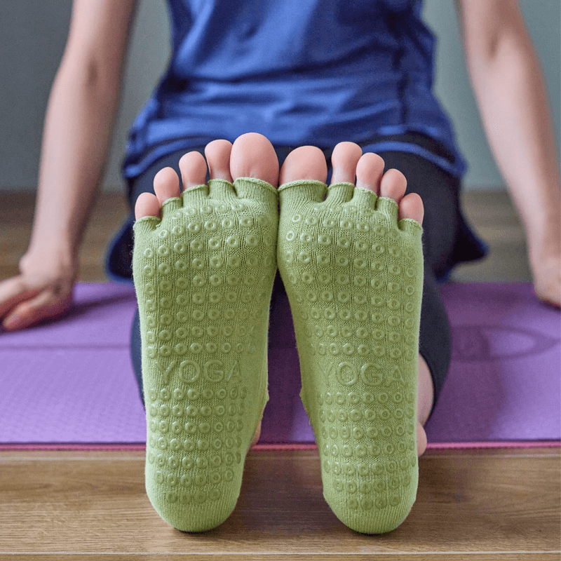 Woman wearing green non-slip five-toe yoga socks on a purple mat, perfect for yoga practice.