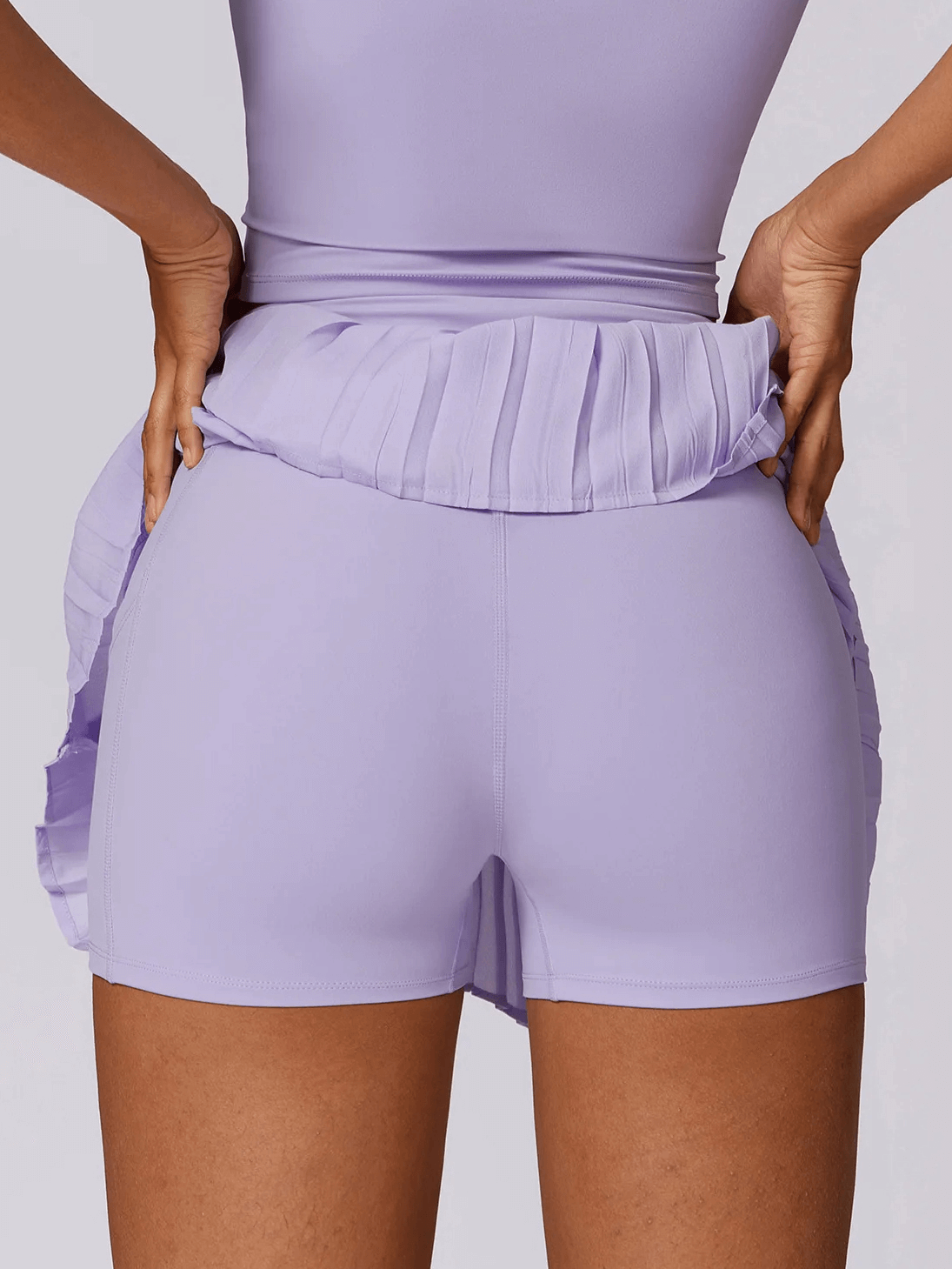 Back view of women's athletic pleated skort in purple, showcasing integrated shorts for style and comfort.