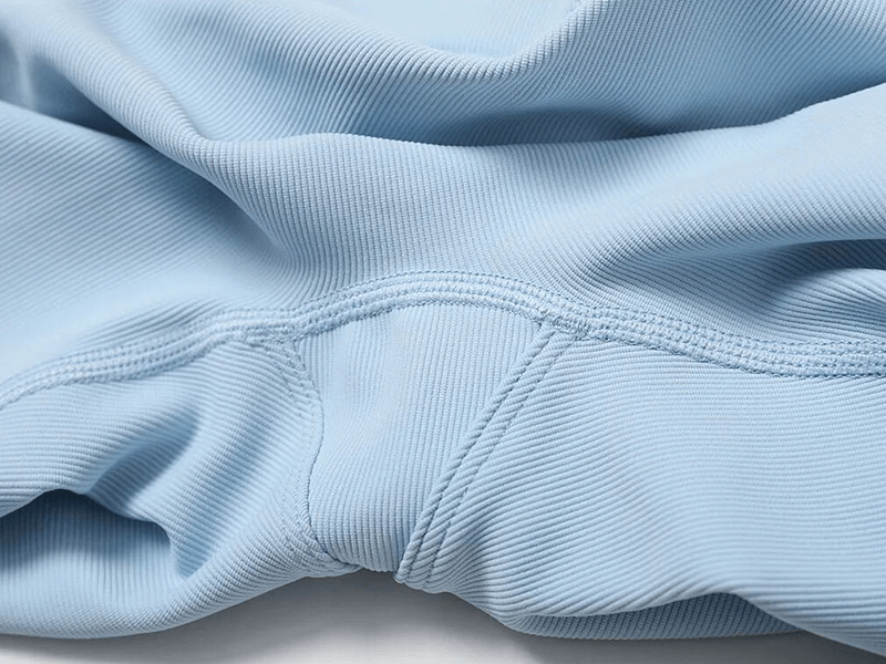 Close-up of light blue ribbed sportswear fabric with stitching detail, showcasing quality and texture for activewear.