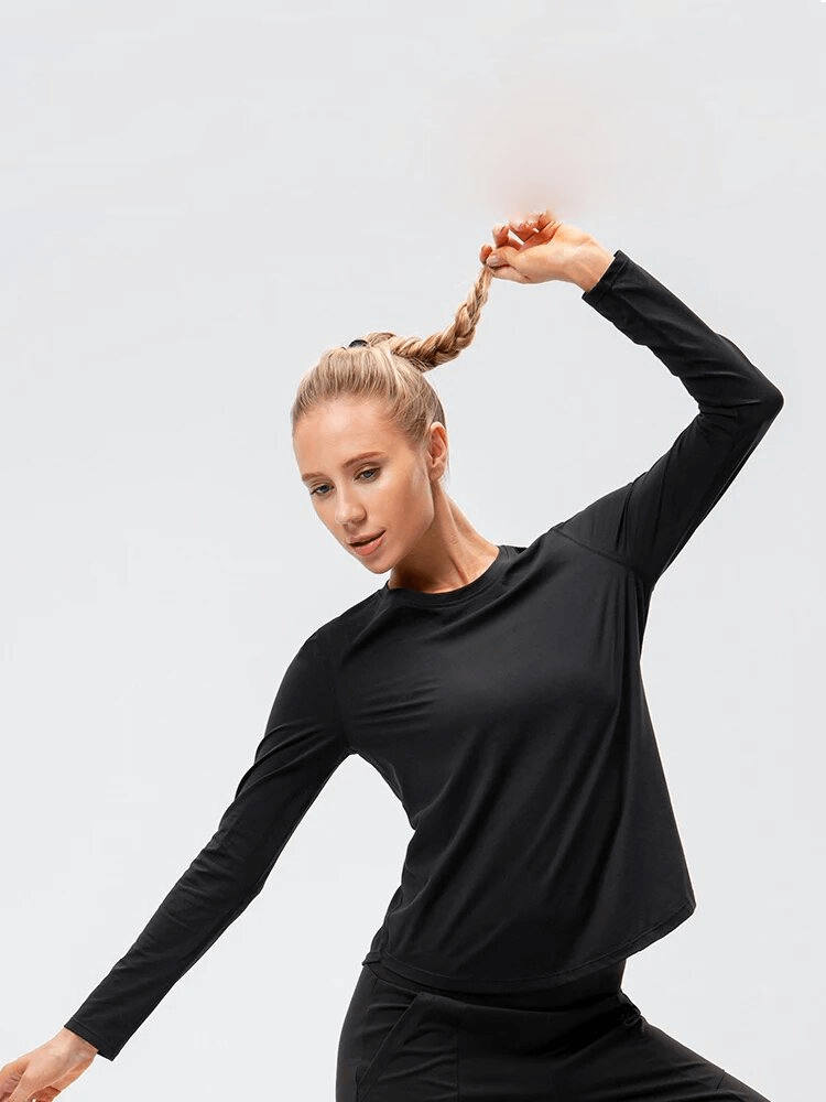 Woman in black long-sleeve sports top doing yoga, showcasing flexibility and comfort of quick-drying, breathable activewear.