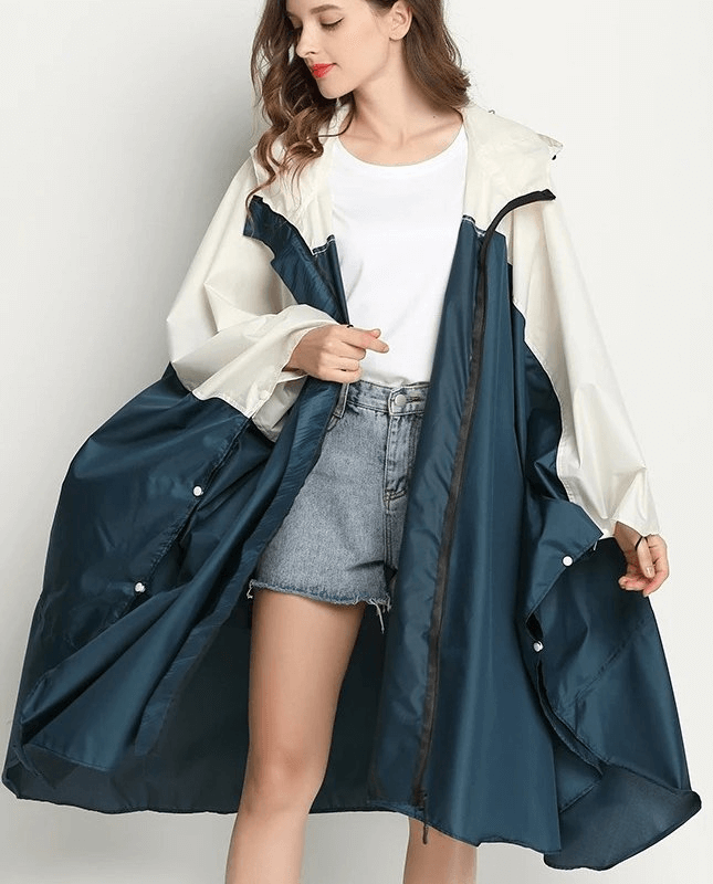 Woman in blue and white raincoat-poncho with hood and zipper, wearing casual outfit, demonstrating waterproof fashion.