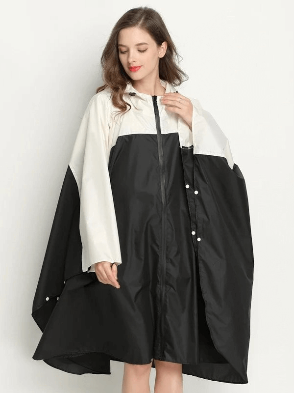 Woman wearing black and white raincoat-poncho with zipper and hood, made of waterproof polyester for rainy days.