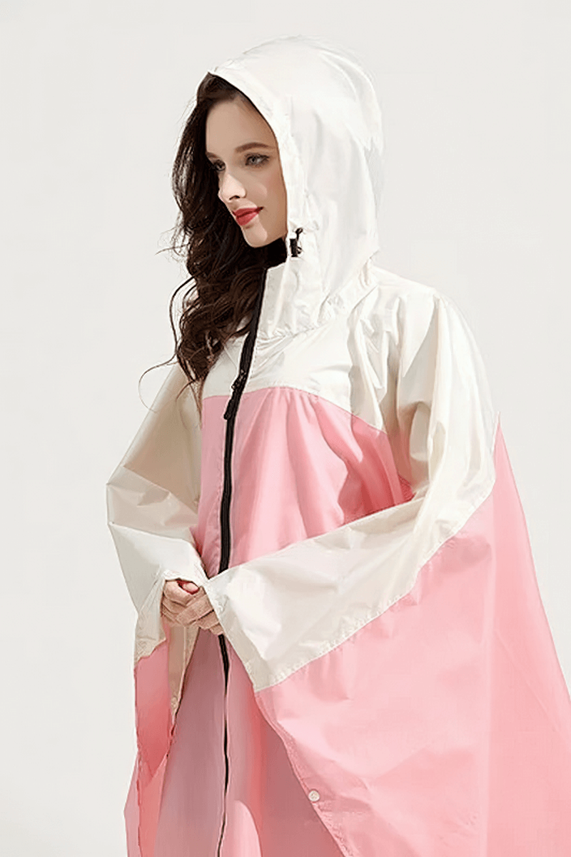 Woman wearing a pink and white waterproof raincoat-poncho with hood and zipper, perfect for rainy days.