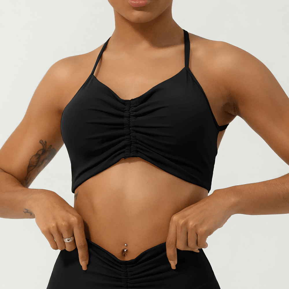 Woman wearing black ruched sports top with strappy back, ideal for active wear and fitness.