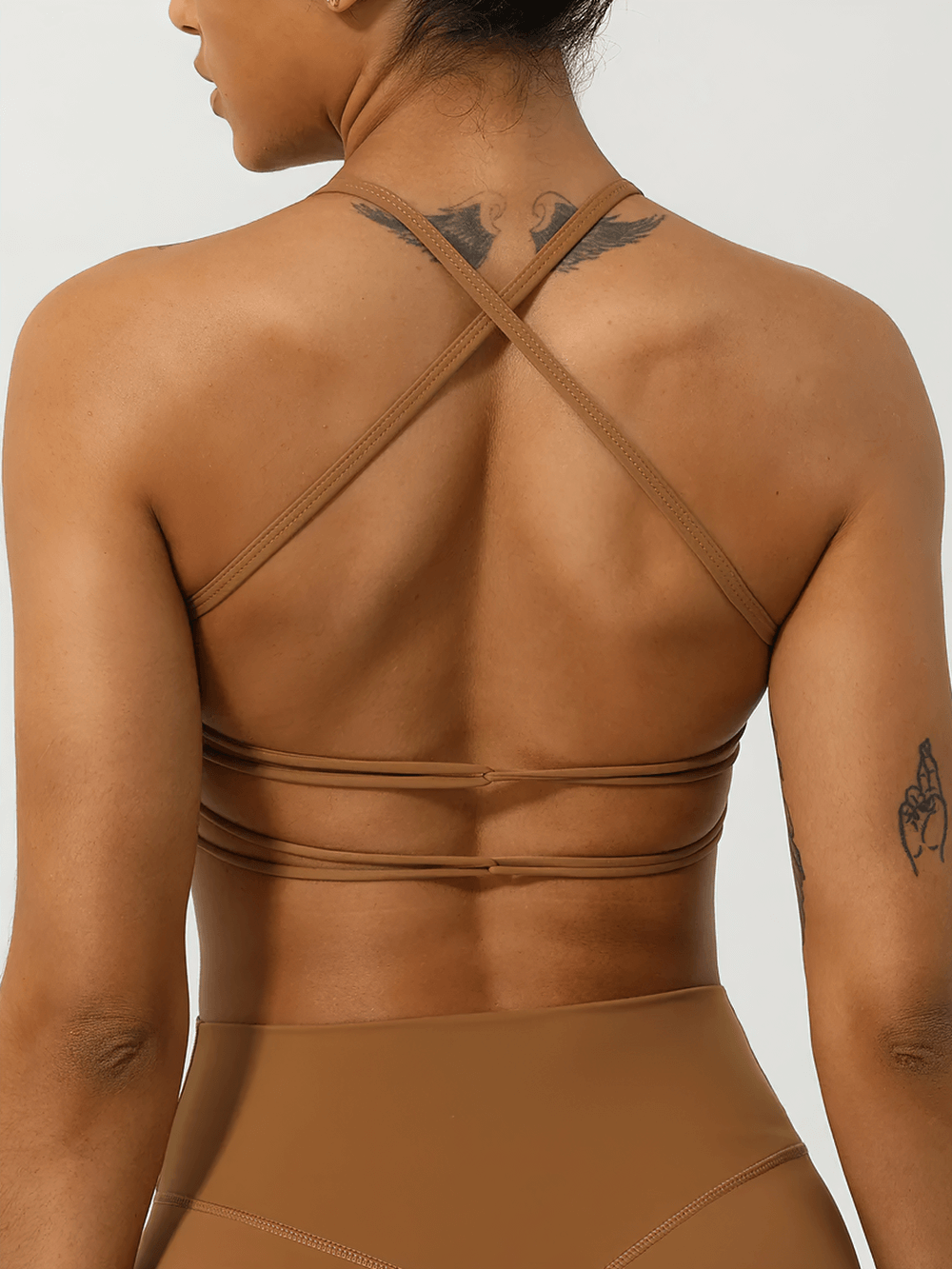 Back view of a woman wearing a brown ruched sports top with strappy back design for fitness, highlighting style and support.