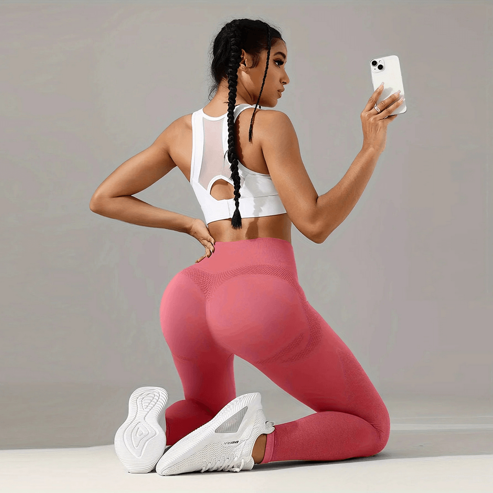 Model wearing Women's Seamless Booty Lift Gym Leggings - SF4059 in pink while holding a smartphone, showcasing squat proof design.