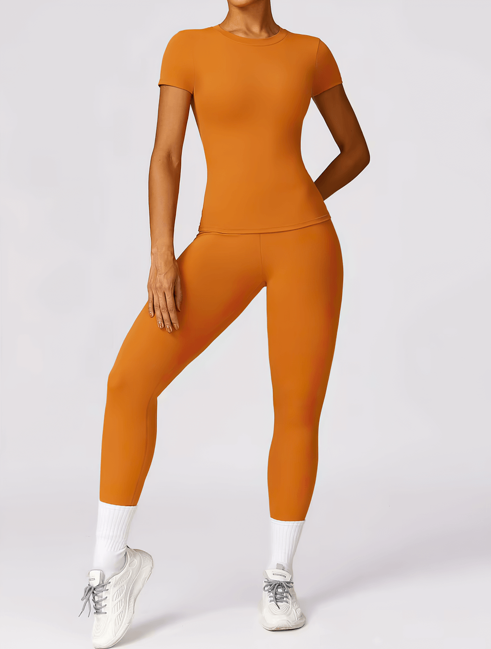 Women's seamless short-sleeve yoga t-shirt in orange, perfect for workouts with quick-dry, breathable fabric. Model in matching leggings.