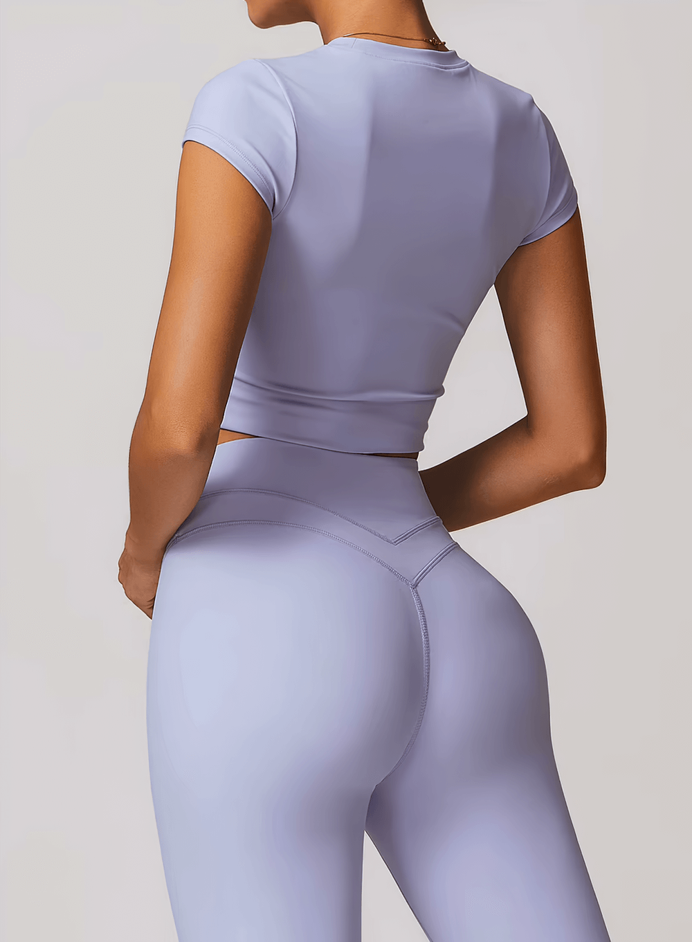 Back view of a woman wearing a lavender short sleeve fitness t-shirt and leggings, perfect for yoga and workouts.