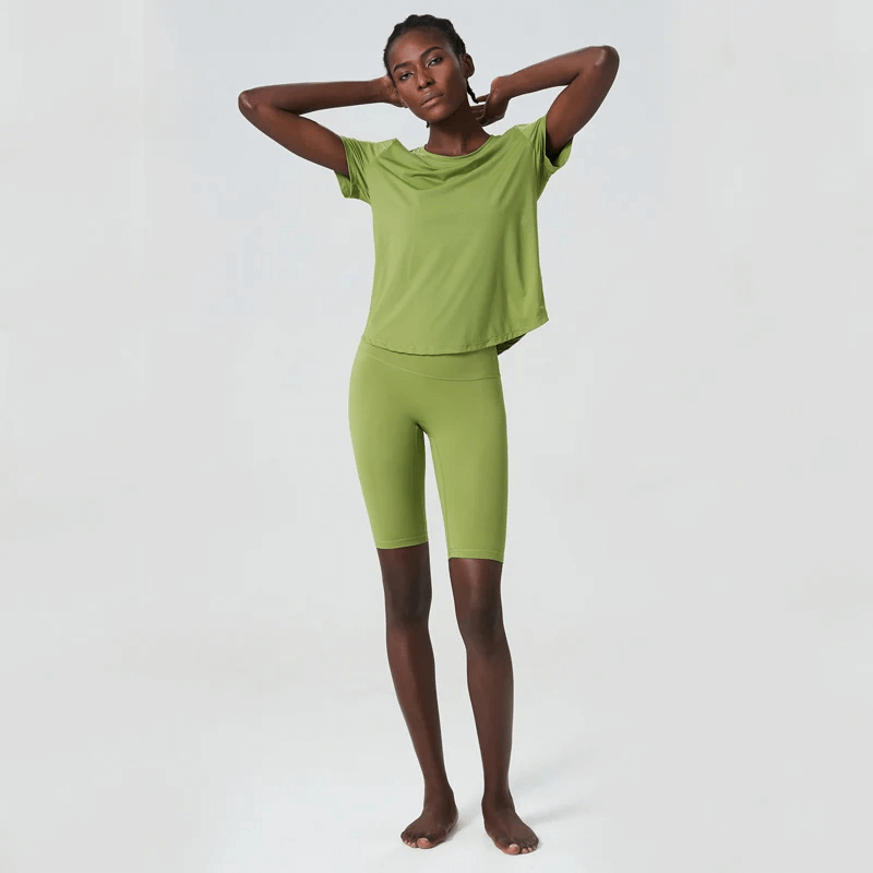 Woman wearing green yoga set, perfect for gym workouts. Solid color, short sleeves, breathable Lycra fabric, anti-shrink and quick-dry.