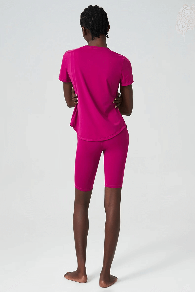 Woman in vibrant pink yoga set made of Lycra, showcasing short sleeves and shorts, perfect for gym and yoga sessions.