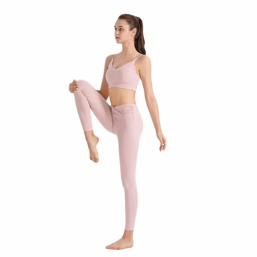 Woman wearing pink spandex workout set doing yoga pose on one leg.
