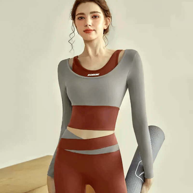 Active woman in grey and red long sleeves crop top, perfect for fitness training and yoga, holding a rolled yoga mat.