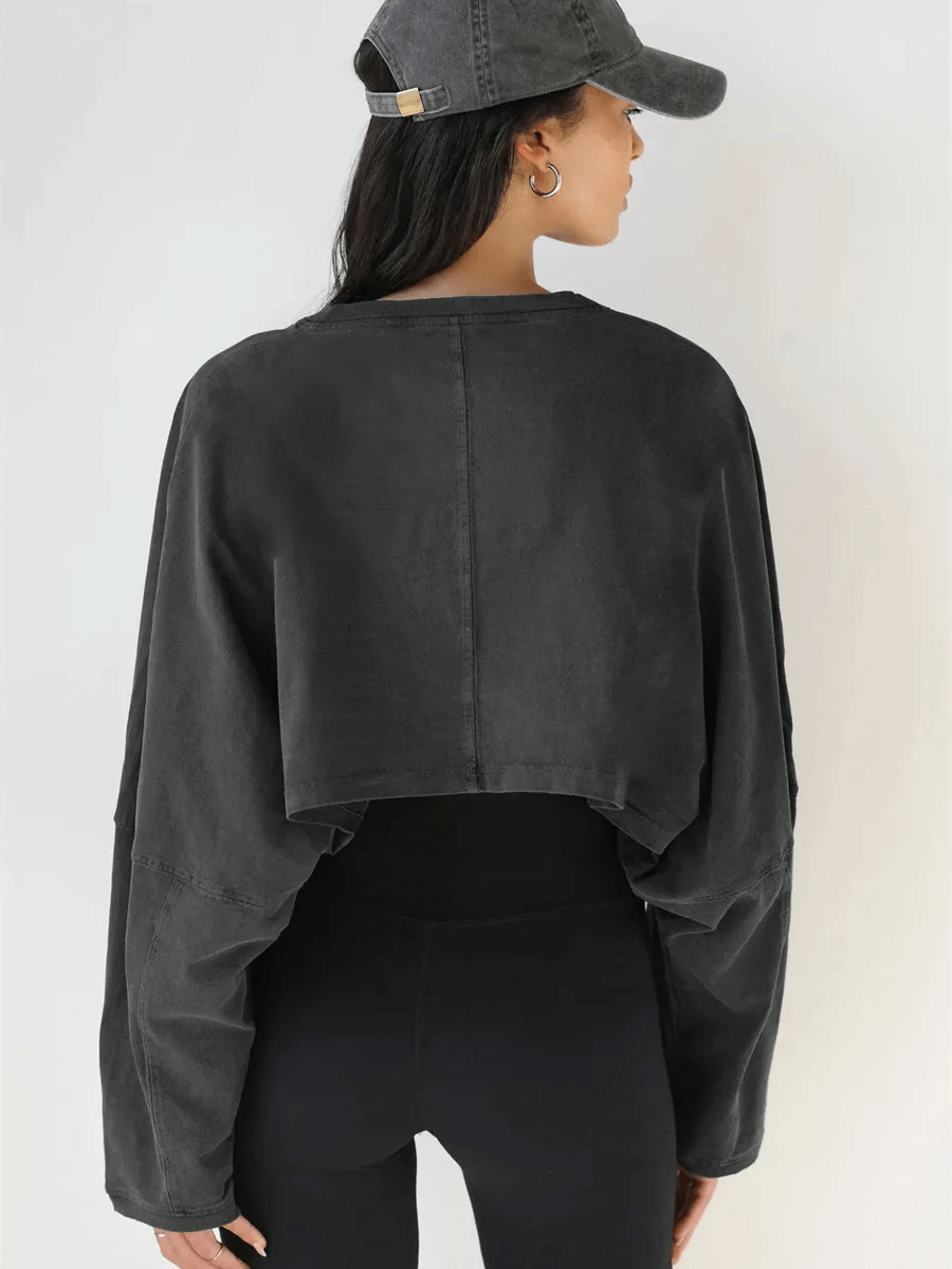 Woman wearing a black loose crop top with long sleeves, perfect for gym workouts and yoga. Athletic and stylish look.