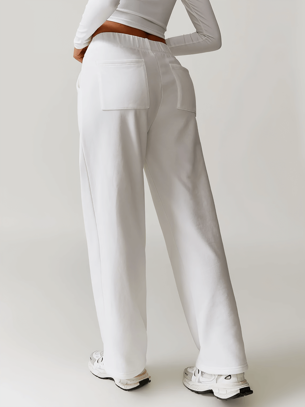 Back view of women's white high-waist straight-leg sweatpants, featuring pockets and paired with sneakers for a casual look.