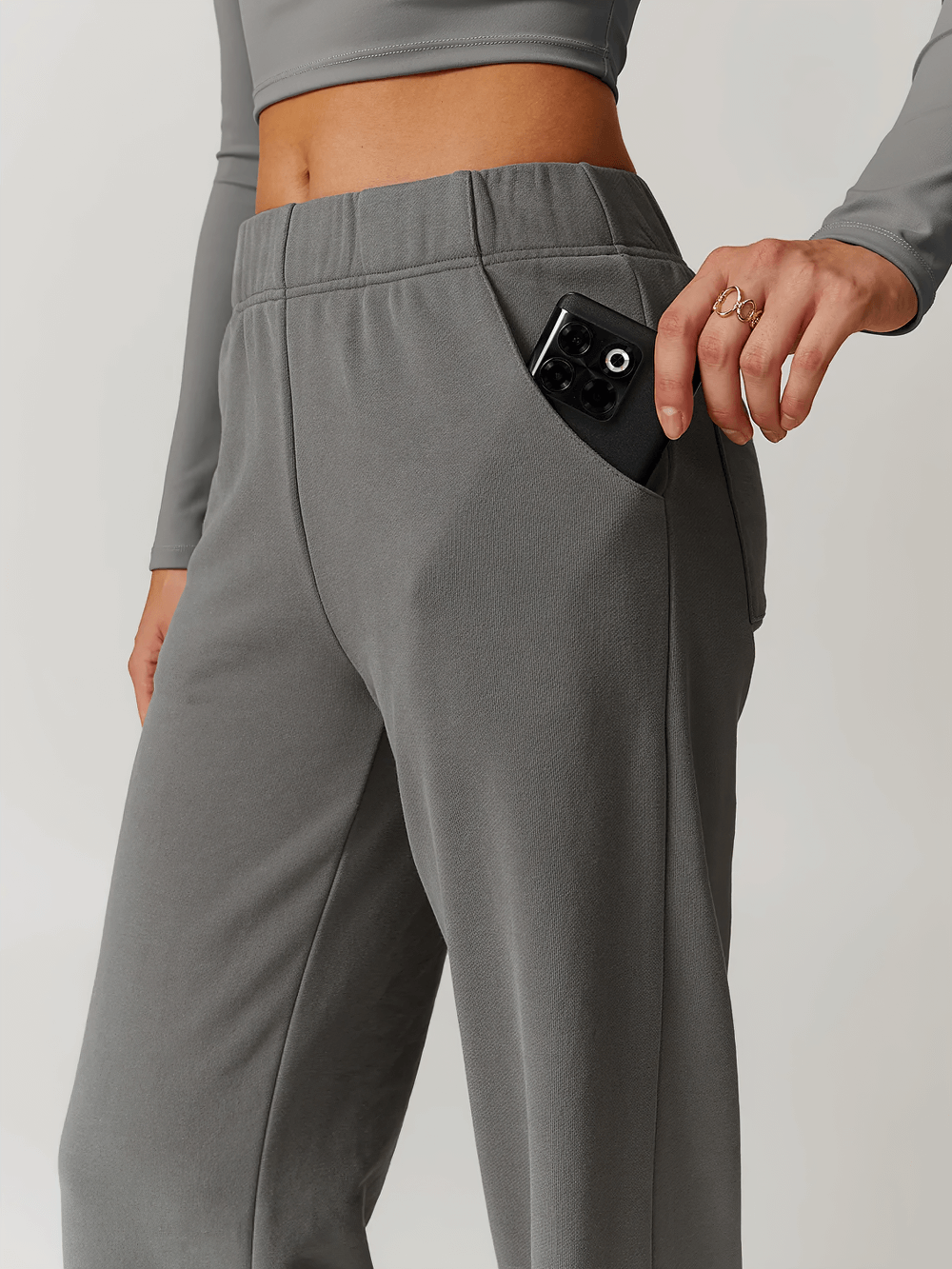 Woman wearing gray high-waisted straight-leg sweatpants with a phone in pocket.