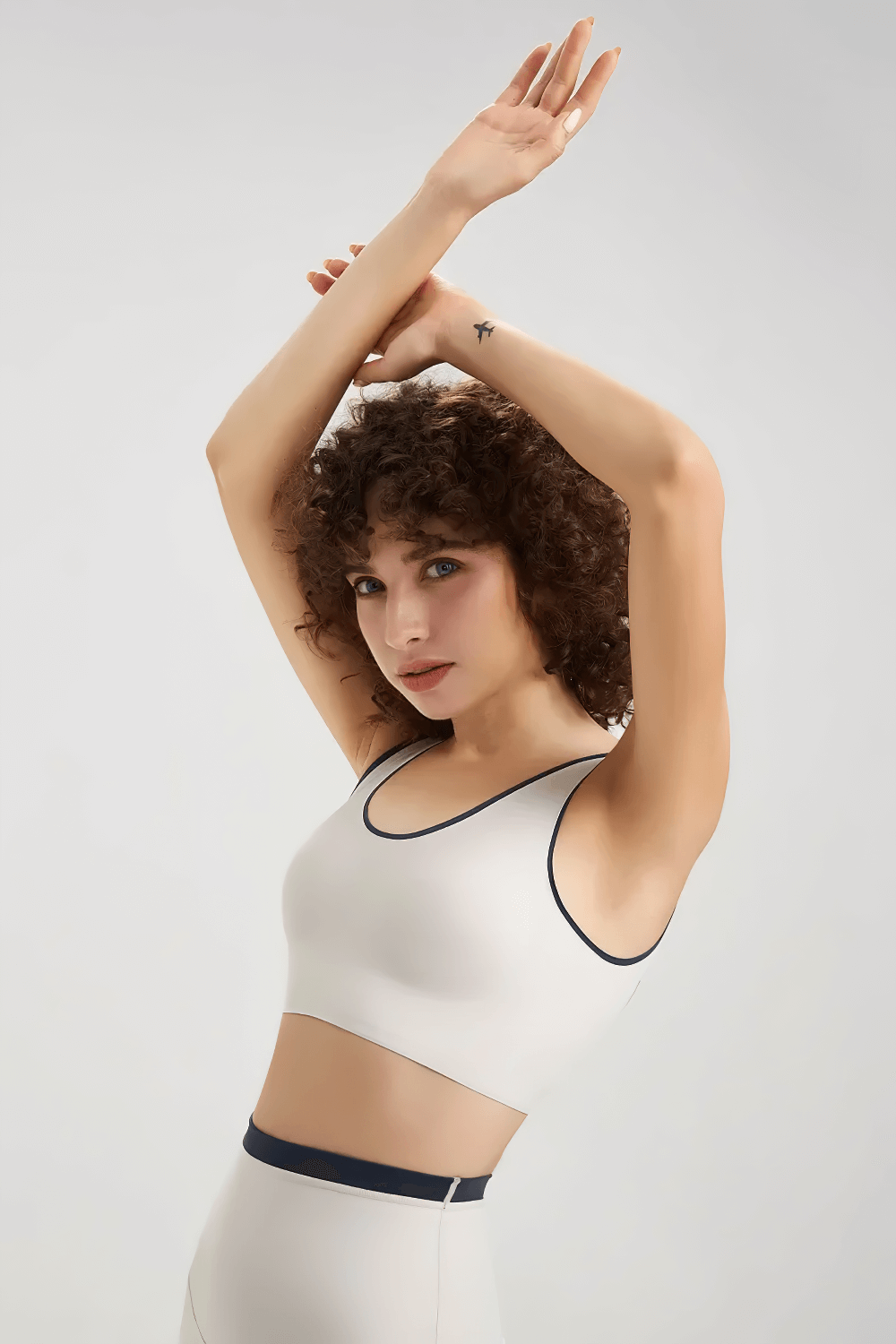 Woman in white seamless yoga sports bra, arms raised, showcasing breathable, stretchy nylon blend. Ideal for running and yoga.