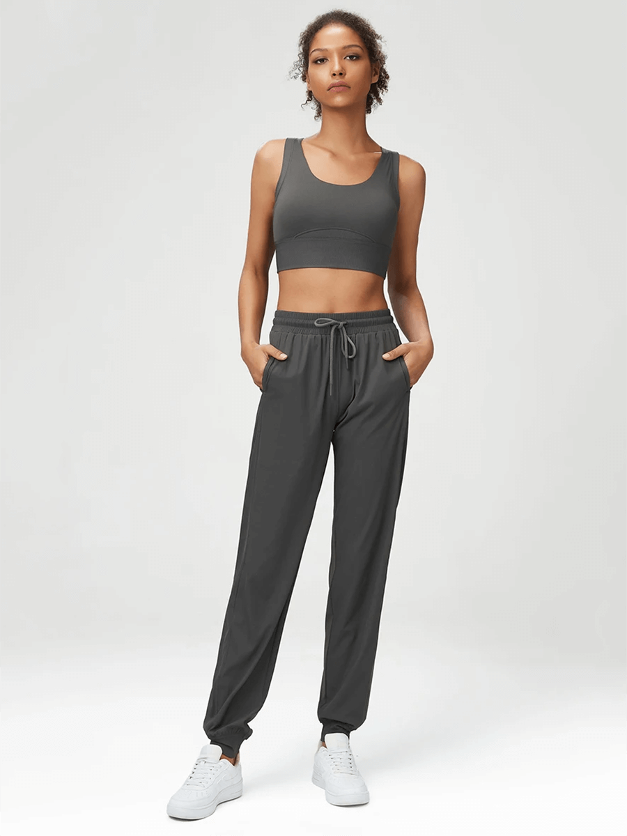 Woman wearing stylish gray joggers and sports bra set with adjustable drawstrings, highlighting fitness fashion and versatility.