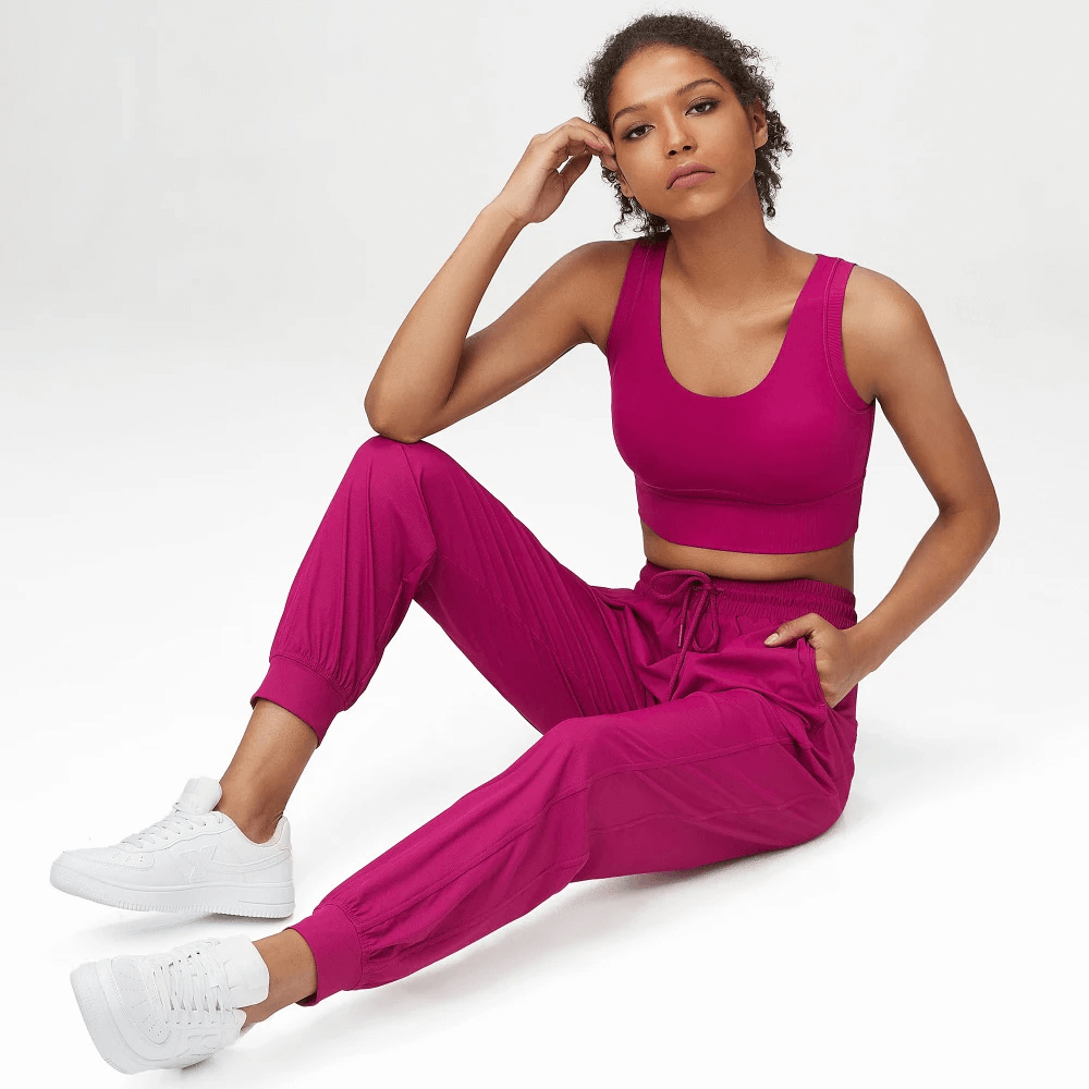 Woman wearing vibrant pink joggers and sports bra set, sitting stylishly. Perfect for active or casual wear. Fitness fashion SF2089.