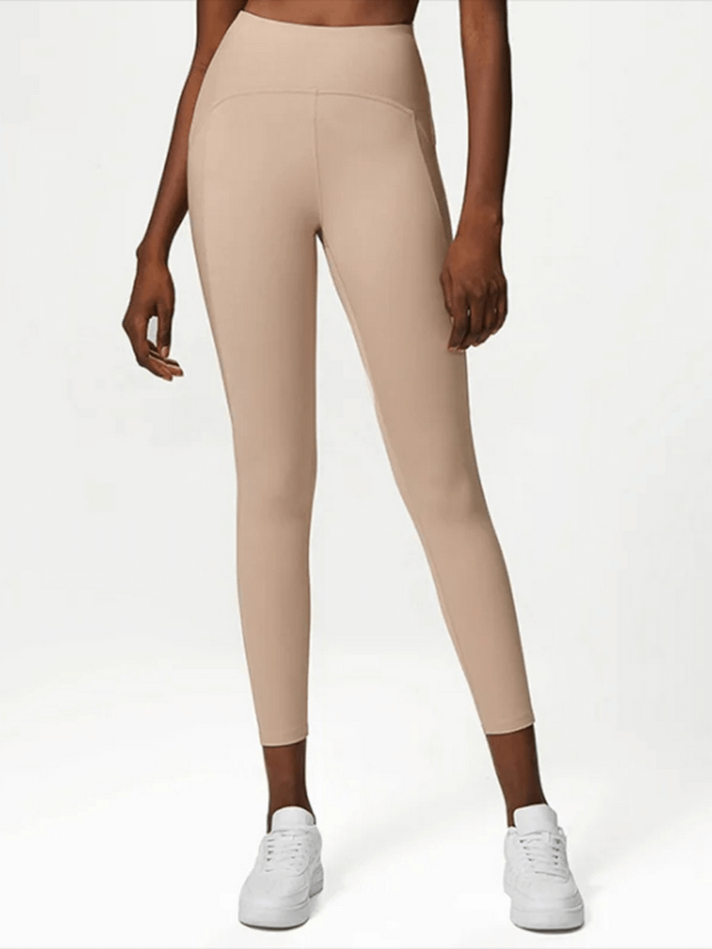 Woman wearing beige nylon-spandex yoga leggings, versatile for gym and running, featuring a strong elastic waistband.