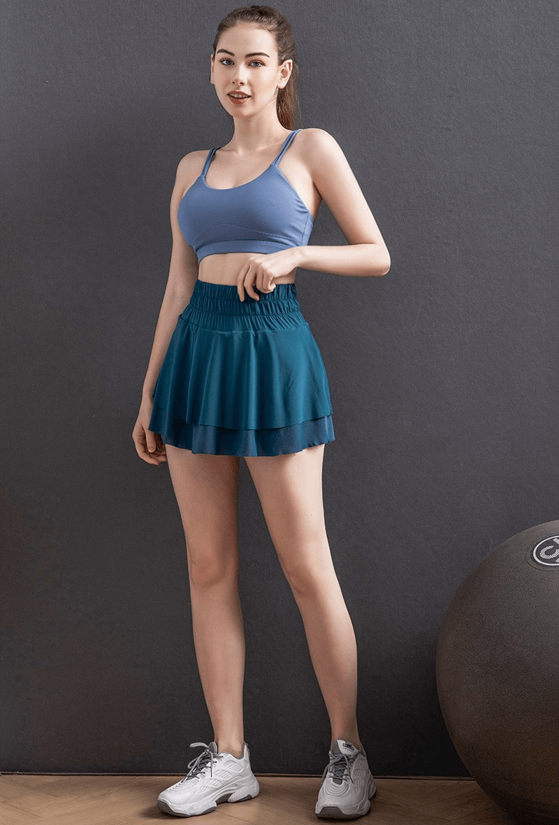 Woman wearing blue high waist tennis skirt with hidden pockets, ideal for sports like yoga and running, showcasing sleek design and comfort.