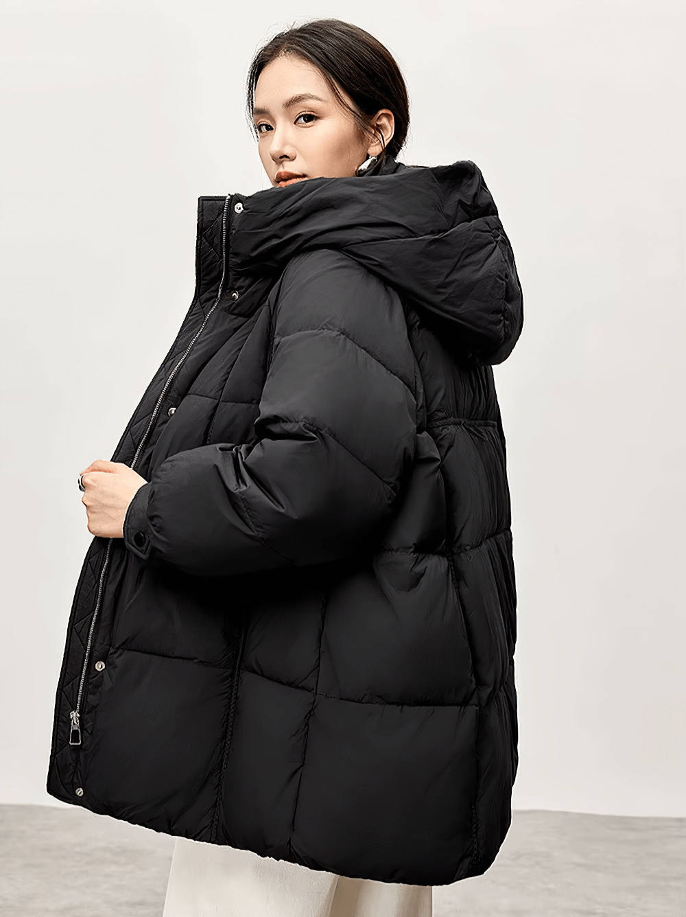 Woman wearing a black hooded duck down puffer jacket, showcasing its warmth and stylish wide-waisted fit. Perfect for winter fashion.