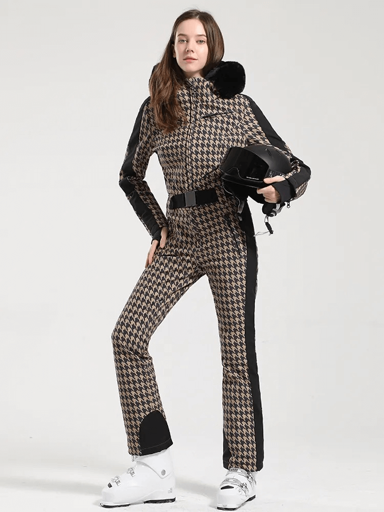 Stylish woman in warm houndstooth ski suit with hood, holding helmet, ready for a day on the slopes.