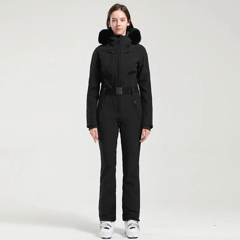 Woman wearing a black one-piece ski suit with hood, ideal for cold weather, featuring waterproof and windproof fabric.